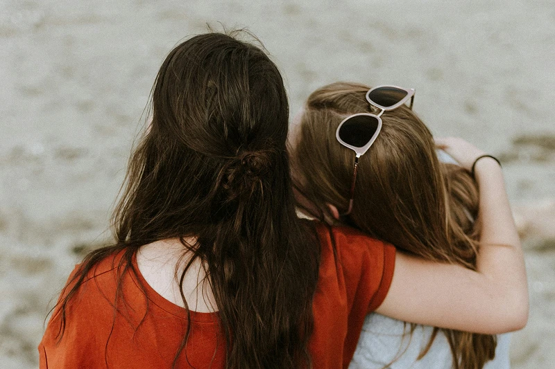 Women sitting on beach hugging